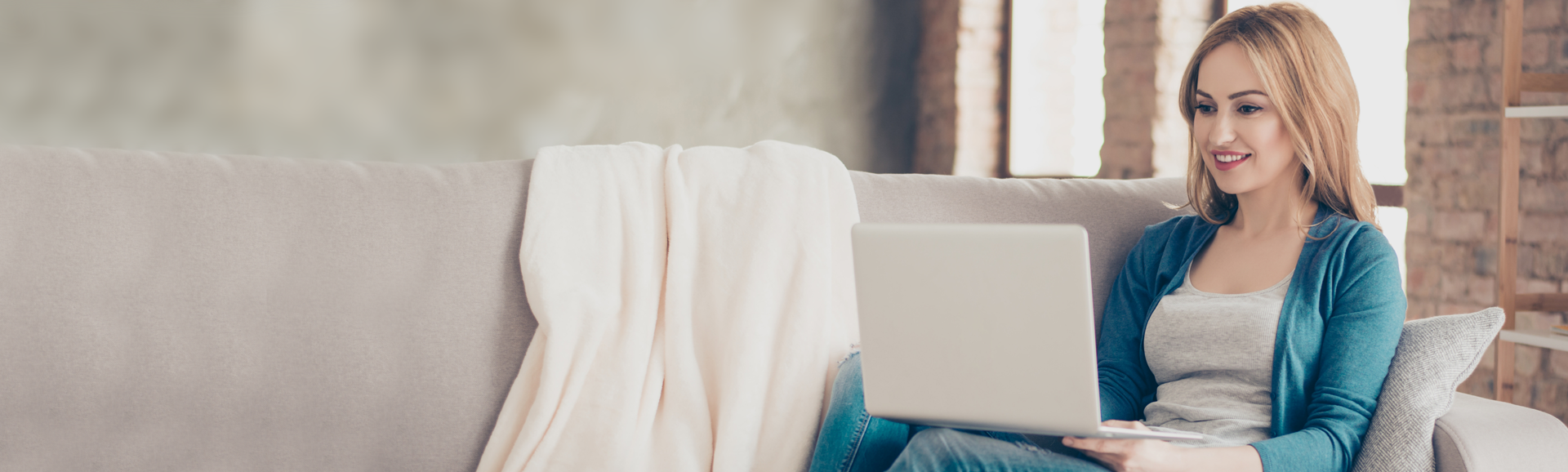 Junge Frau auf dem Sofa sitzend mit einem Laptop auf den Knien.